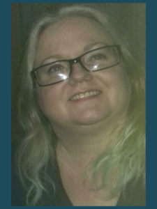 Suzy Molloy is wearing balck framed glasses and looking up to the left, smiling