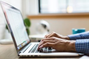 you can see male hands typing on a laptop, but you can't see the screen to see what he is typing