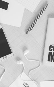 eBook Creation, is turning your words, text and images into a digital file.
Image shows a desktop with a smartphone, scattered papers, earphones, a pen and a printed booklet in black and white.