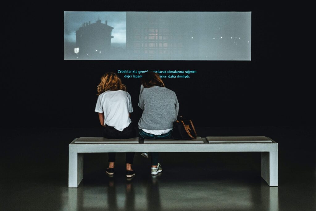 Two people on a bench in front of a video screen with subtitles, highlighting the significance of transcripts for accessibility and growing global audience reach.